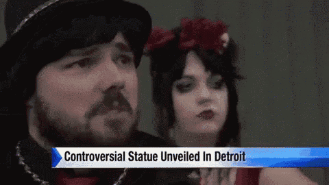 a man and a woman are standing next to each other with a sign that says controversial statue unveiled in detroit .