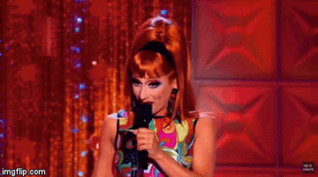 a woman with red hair is holding a microphone in front of a red curtain .