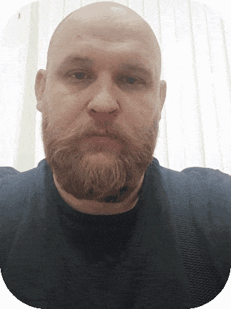 a bald man with a beard wearing a black shirt looks at the camera