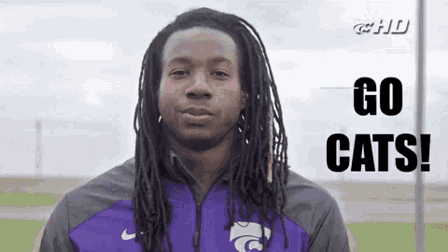 a man with long dreadlocks is wearing a purple jacket and says go cats .