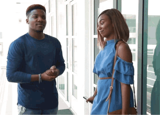 a man in a blue shirt and a woman in a blue dress are standing next to each other in a hallway