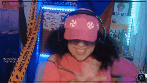 a woman wearing a pink hat and headphones is smiling in front of a warning tape that says halloween