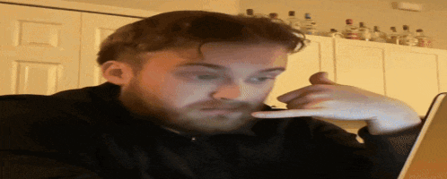 a man with a beard is sitting in front of a laptop making a call me gesture