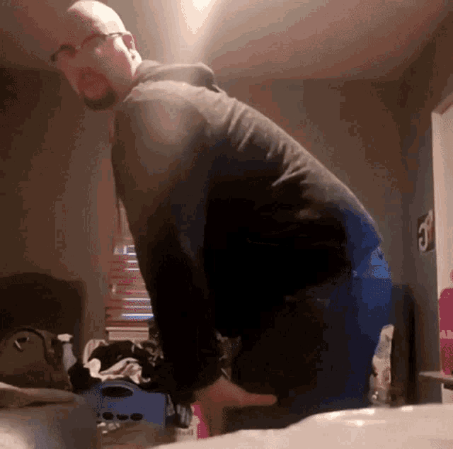 a man with glasses and a beard is standing on a bed in a bedroom