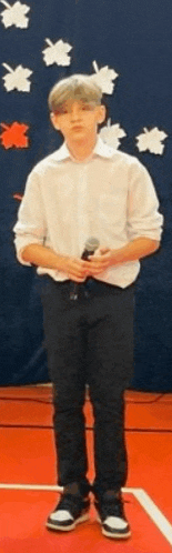 a young boy in a white shirt and black pants is holding a microphone while standing on a basketball court .