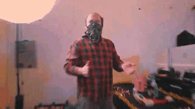 a man wearing a plaid shirt and a gas mask is dancing in a room .