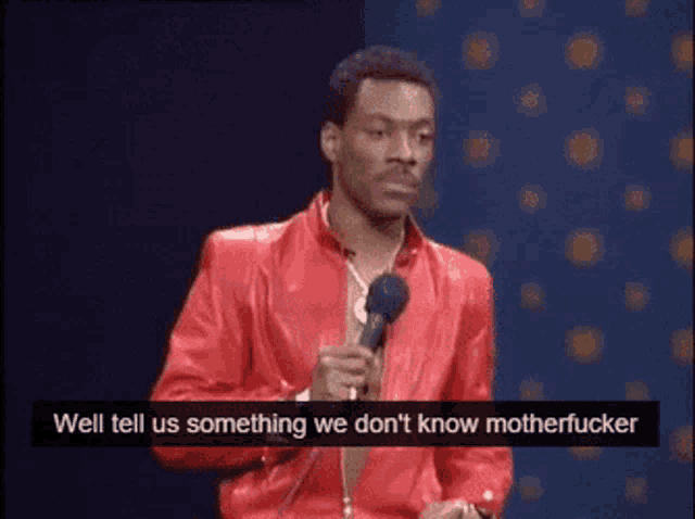 a man in a red jacket is holding a microphone and saying " well tell us something we don 't know motherfucker "