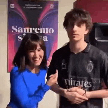 a man and a woman are posing for a picture in front of a poster .