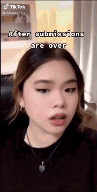 a girl is wearing a black shirt and a heart necklace while making a funny face .