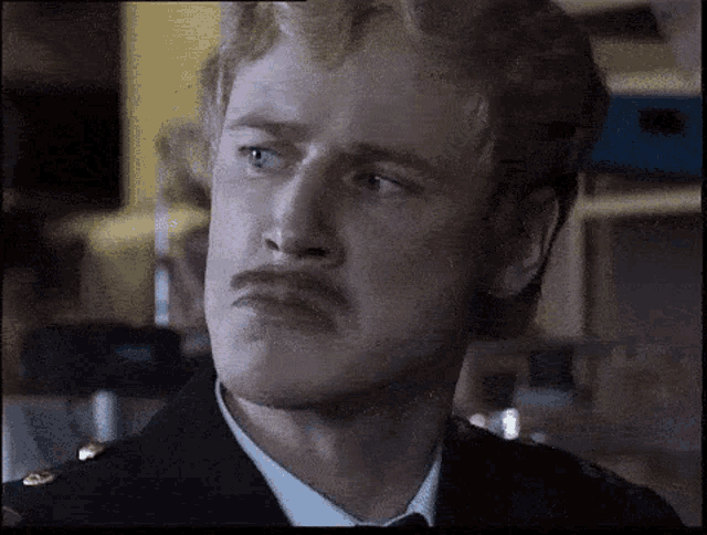 a man with a mustache is wearing a uniform and making a face .