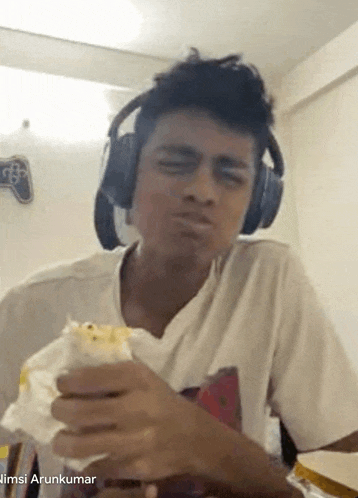 a young man wearing headphones is eating a sandwich while making a funny face