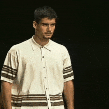 a man in a white shirt with brown stripes on the sleeves is standing in front of a black background