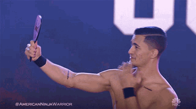 a shirtless man is taking a picture of himself in a mirror with a nbc logo in the background