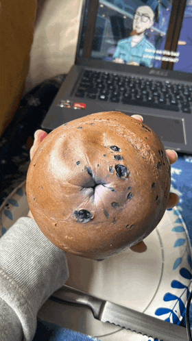 a person is holding a doughnut in front of a laptop