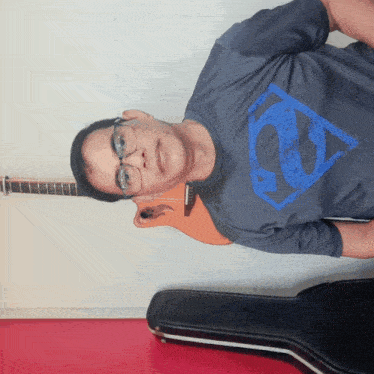 a man wearing glasses and a superman shirt holds a guitar