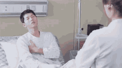 a man is sitting in a hospital bed with his arms crossed and talking to a doctor .