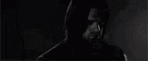 a man with long hair and a beard is standing in a dark room .