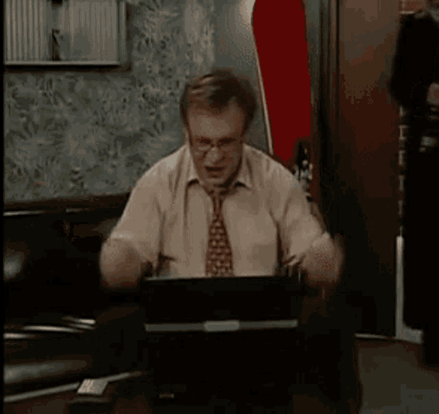 a man in a tie is sitting in front of a laptop computer and holding a drink .