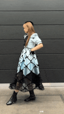 a woman in a blue dress and black boots is standing in front of a wall that says ' aoyama ' on it