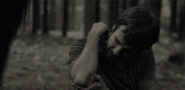 a man is laying on the ground in the woods holding his elbow in pain