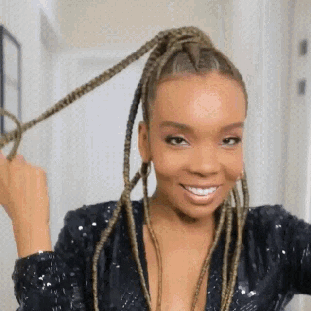 a woman in a black sequined top has braids in her hair and is smiling