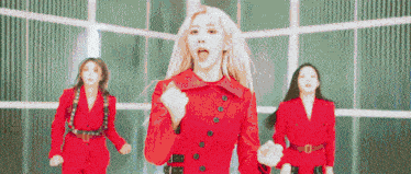 a group of women in red suits are dancing in front of a building .