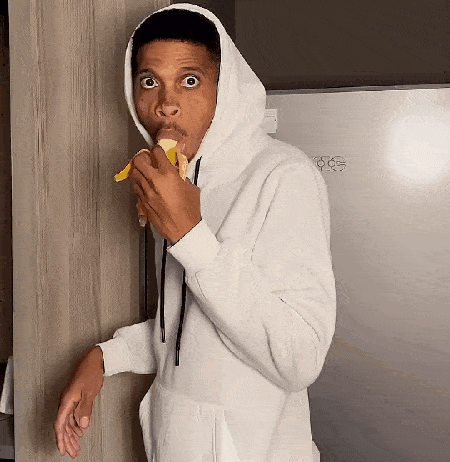 a man wearing a hoodie is eating a banana