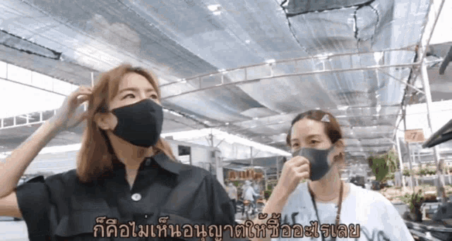 two women wearing face masks are standing in a market