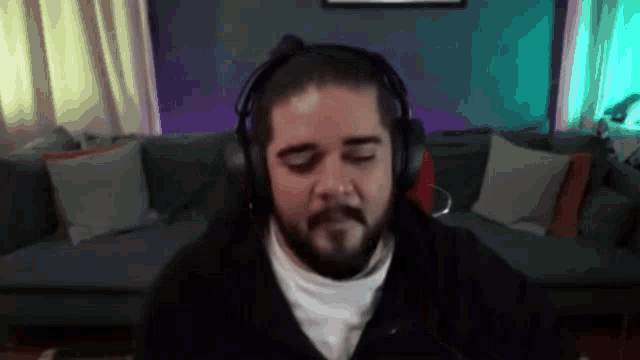 a man with a beard is wearing headphones while sitting in front of a couch .
