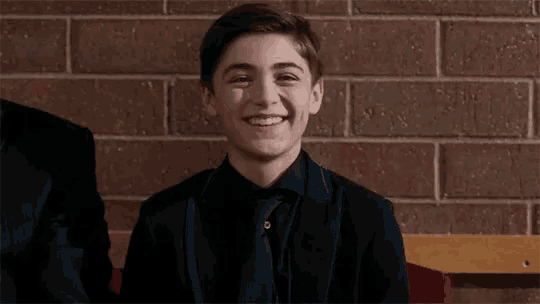 a young man in a suit and tie is smiling while sitting on a bench .
