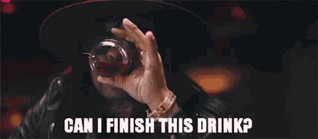 a man in a hat is holding a glass of red liquid and says can i finish this drink .