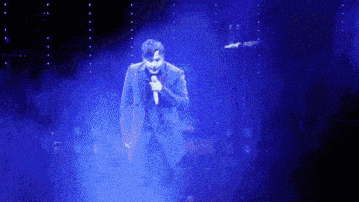 a man in a suit is singing into a microphone on a stage with blue lights behind him