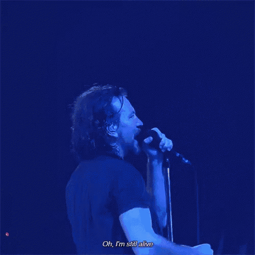 a man singing into a microphone with the words oh , i 'm still alive below him