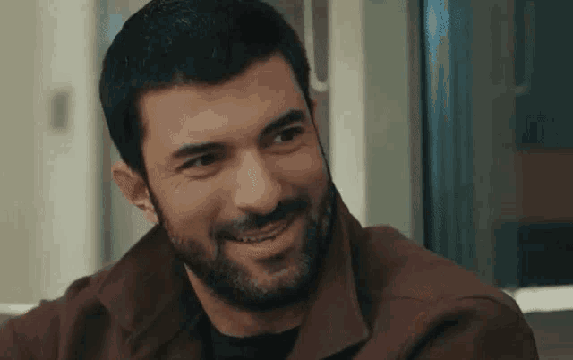 a man with a beard is smiling and wearing a brown shirt .