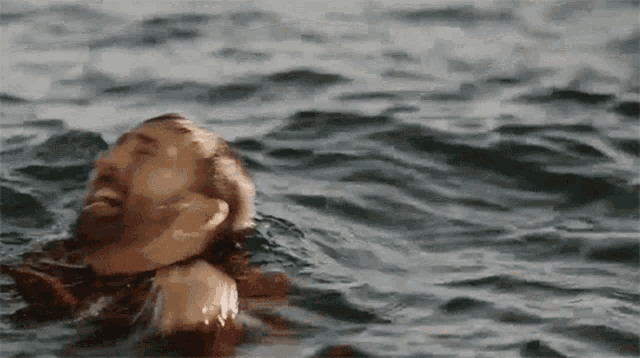 a man with a beard is swimming in the ocean with his head above the water .