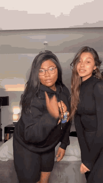 two women are standing next to each other in a bedroom