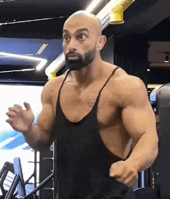 a bald man with a beard is standing in a gym wearing a tank top .