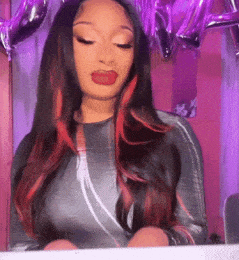 a woman with long hair and red highlights is standing in front of balloons and a mirror .