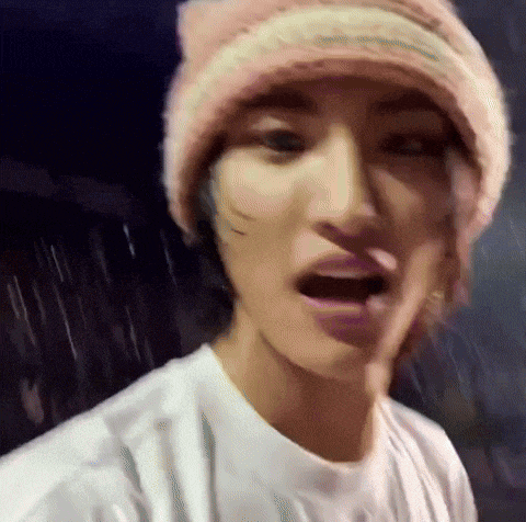 a man wearing a pink beanie and a white shirt is standing in the rain .