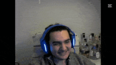 a man wearing blue headphones is smiling while sitting in front of a table filled with bottles of alcohol .