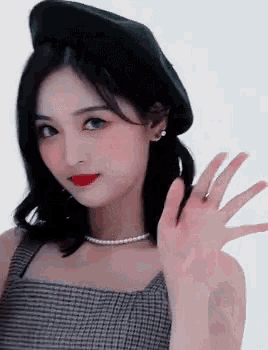a young woman wearing a beret and a pearl necklace is waving her hand .