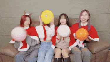 four girls are sitting on a couch and holding balloons