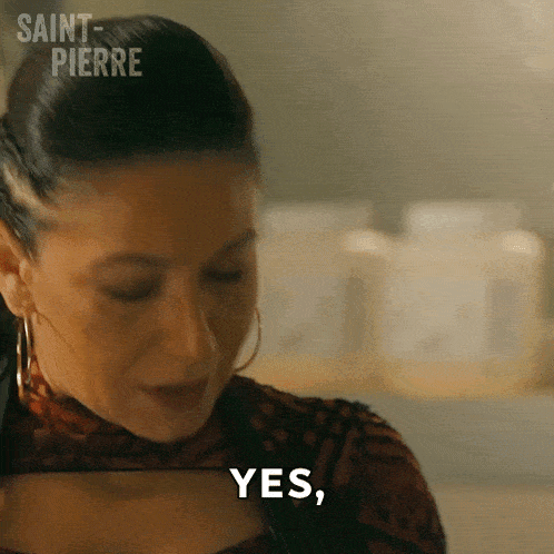 a woman is smiling and saying yes in front of a shelf of bottles .
