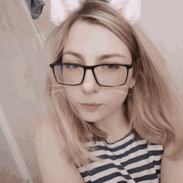 a woman wearing glasses and a striped shirt has a cat filter on her face