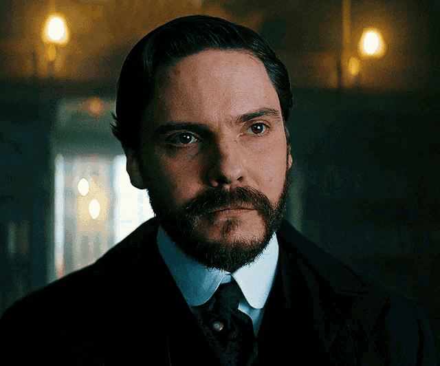 a man with a beard wearing a suit and tie looks at the camera