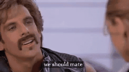 a man with a mustache is smiling while talking to another man .