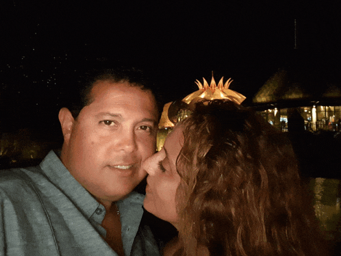a woman kisses a man on the cheek in front of a thatched hut at night
