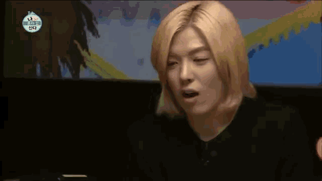 a man with blonde hair is sitting in front of a television .