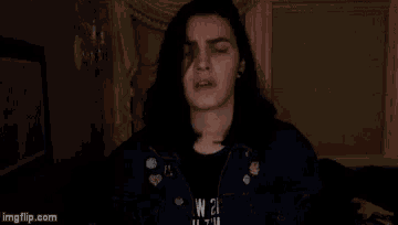 a young man with long hair is wearing a denim jacket and looking at the camera .