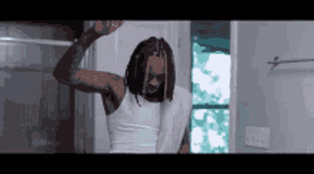 a man in a white tank top is standing in a bathroom with a towel around his neck .